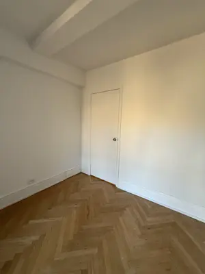 Completed herringbone hardwood floor installation in bright NYC apartment room with white walls