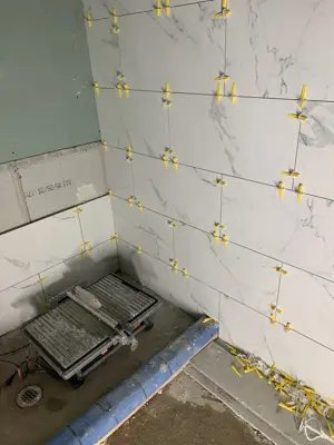 large format marble-look tiles being set with leveling clips and tile saw in shower area nyc