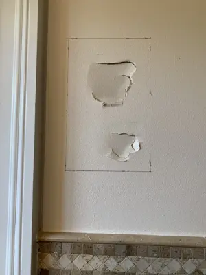 two damaged drywall holes marked for repair on a bathroom wall above tile in nyc home
