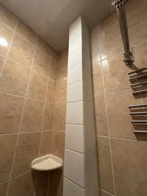 finished bathroom corner column with white accent tiles contrasting warm beige wall tiles in nyc