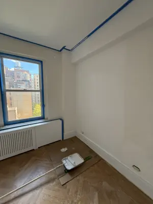 Room painting in progress with blue painter's tape applied along ceiling and window trim in NYC apartment