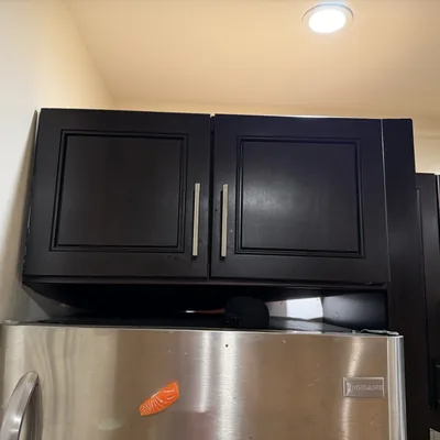 Dark upper kitchen cabinet mounted above a refrigerator