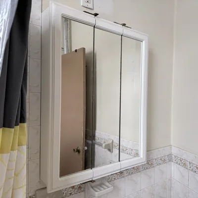 Tri-fold mirrored medicine cabinet mounted on a tiled bathroom wall